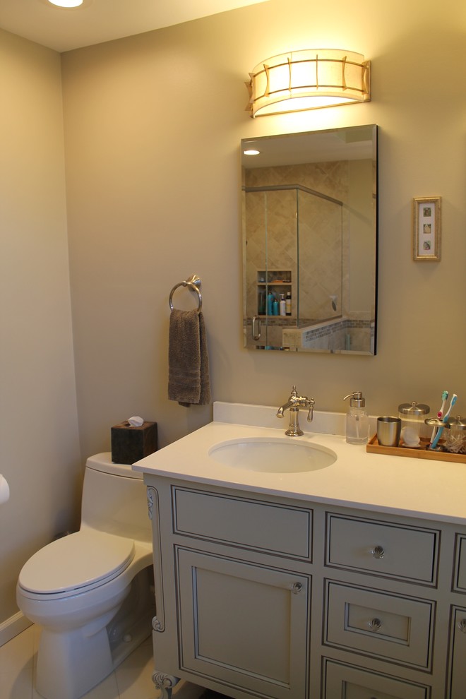Mid-sized transitional 3/4 beige tile and travertine tile travertine floor and beige floor tub/shower combo photo in New York with beaded inset cabinets, gray cabinets, a one-piece toilet, beige walls, an undermount sink, solid surface countertops, a hinged shower door and white countertops