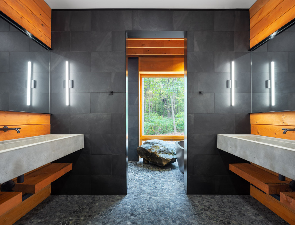 На фото: большая главная ванная комната в стиле модернизм с серыми фасадами, отдельно стоящей ванной, душевой комнатой, унитазом-моноблоком, серой плиткой, плиткой из сланца, серыми стенами, полом из галечной плитки, монолитной раковиной, столешницей из бетона, серым полом, открытым душем и серой столешницей