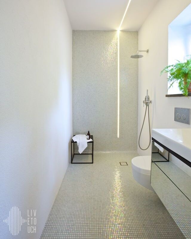 Bild på ett industriellt badrum, med vita väggar, mosaikgolv, luckor med glaspanel, skåp i mellenmörkt trä, en hörndusch, en vägghängd toalettstol, vit kakel, glaskakel, ett integrerad handfat och bänkskiva i glas