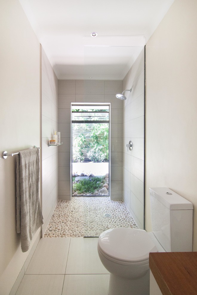 Modernes Badezimmer mit offener Dusche, Wandtoilette mit Spülkasten, beigen Fliesen, beiger Wandfarbe, Kiesel-Bodenfliesen, beigem Boden und offener Dusche in Sonstige