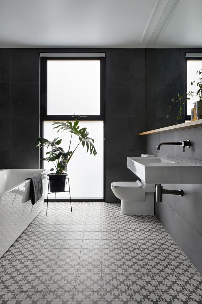 Стильный дизайн: большая главная ванная комната в стиле модернизм с плоскими фасадами, светлыми деревянными фасадами, отдельно стоящей ванной, открытым душем, унитазом-моноблоком, серой плиткой, керамогранитной плиткой, подвесной раковиной, черными стенами, полом из цементной плитки и серым полом - последний тренд