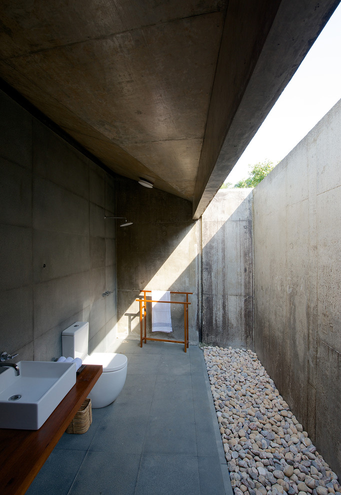 Cette photo montre une salle de bain longue et étroite moderne de taille moyenne avec un plan de toilette en bois, WC à poser, un carrelage gris, des carreaux de béton, une vasque, une douche à l'italienne et un plan de toilette marron.