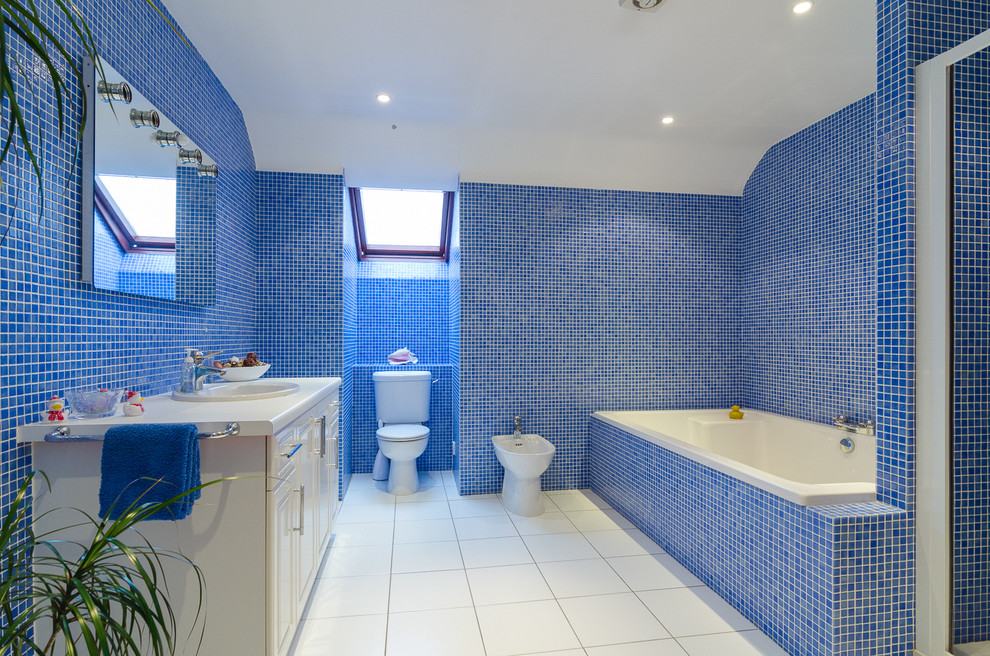 Идея дизайна: ванная комната: освещение в современном стиле с фасадами с выступающей филенкой, белыми фасадами, накладной ванной, биде, синей плиткой, плиткой мозаикой и синими стенами