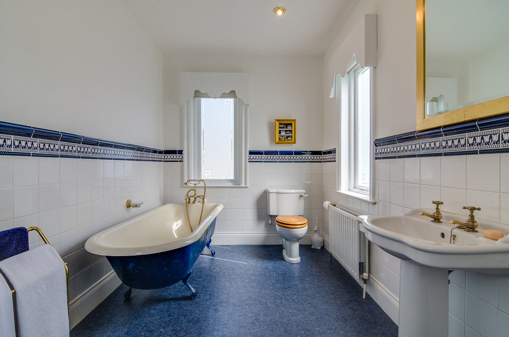 Modelo de cuarto de baño mediterráneo con lavabo con pedestal, bañera con patas, sanitario de dos piezas, paredes blancas y aseo y ducha