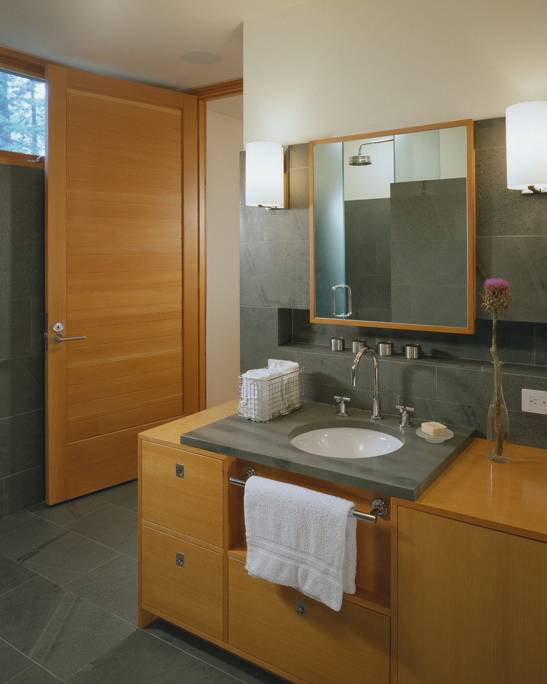 Modern inredning av ett badrum, med ett undermonterad handfat, släta luckor, skåp i mellenmörkt trä, grå kakel och skifferkakel