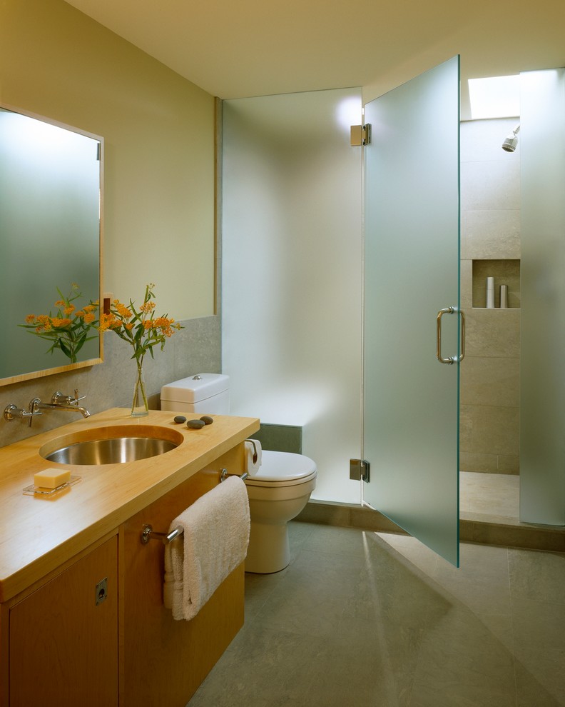 Small modern shower room bathroom in Portland Maine with a submerged sink, flat-panel cabinets, light wood cabinets, wooden worktops, an alcove shower, a two-piece toilet, grey tiles, stone tiles, green walls and limestone flooring.