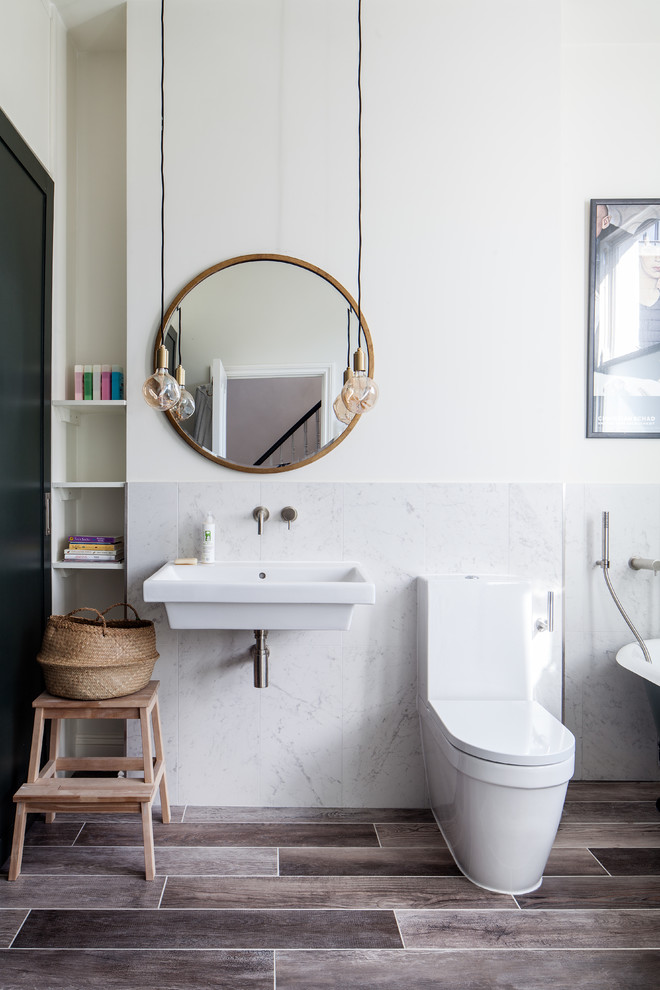 Modelo de cuarto de baño tradicional renovado con bañera con patas, combinación de ducha y bañera, sanitario de una pieza, baldosas y/o azulejos blancos, baldosas y/o azulejos de mármol, paredes blancas, aseo y ducha, lavabo suspendido, suelo marrón y espejo con luz