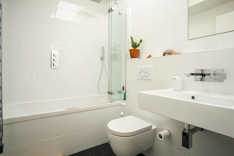 Exemple d'une salle de bain tendance de taille moyenne pour enfant avec une baignoire posée, un combiné douche/baignoire, WC à poser, un carrelage blanc, un mur blanc, un sol noir, une cabine de douche à porte coulissante et un lavabo suspendu.