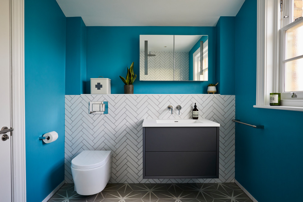 Idée de décoration pour une grande salle de bain design pour enfant avec un placard à porte plane, des portes de placard noires, WC suspendus, un carrelage blanc, des carreaux de porcelaine, un mur bleu, un sol en carrelage de porcelaine, un lavabo intégré, un sol gris et un plan de toilette blanc.