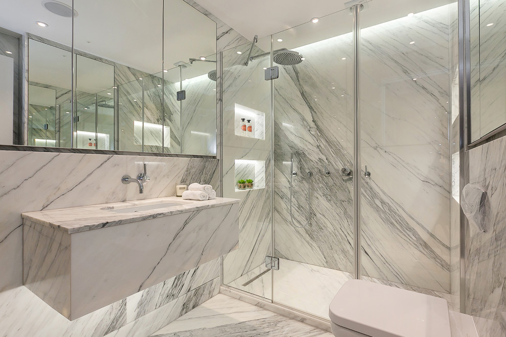 This is an example of a contemporary shower room bathroom in London with an alcove shower, a wall mounted toilet, white tiles, marble tiles, marble flooring, a submerged sink, marble worktops, white floors and a hinged door.