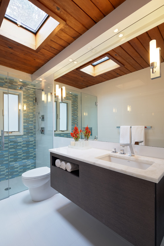 This is an example of a contemporary bathroom in New York with flat-panel cabinets, white cabinets, a corner shower, a one-piece toilet, white walls and a submerged sink.