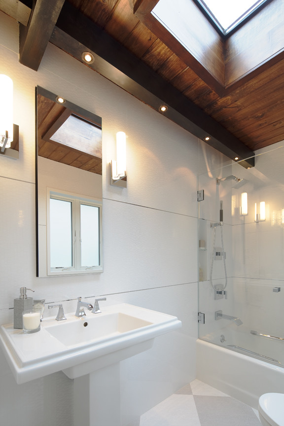 Ejemplo de cuarto de baño principal actual de tamaño medio con bañera esquinera, combinación de ducha y bañera, sanitario de una pieza, baldosas y/o azulejos blancos, paredes blancas y lavabo con pedestal