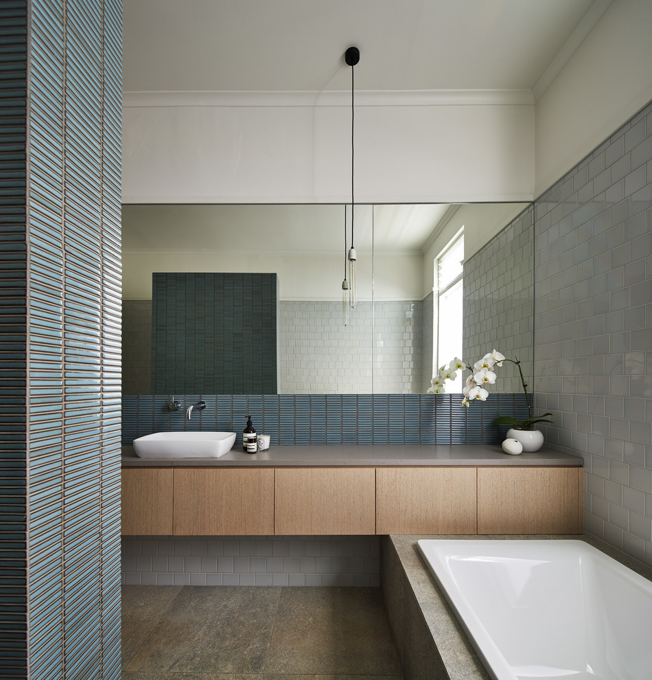 This is an example of a contemporary bathroom in Melbourne with a vessel sink, flat-panel cabinets, light wood cabinets, a built-in bath, blue tiles, matchstick tiles and grey walls.