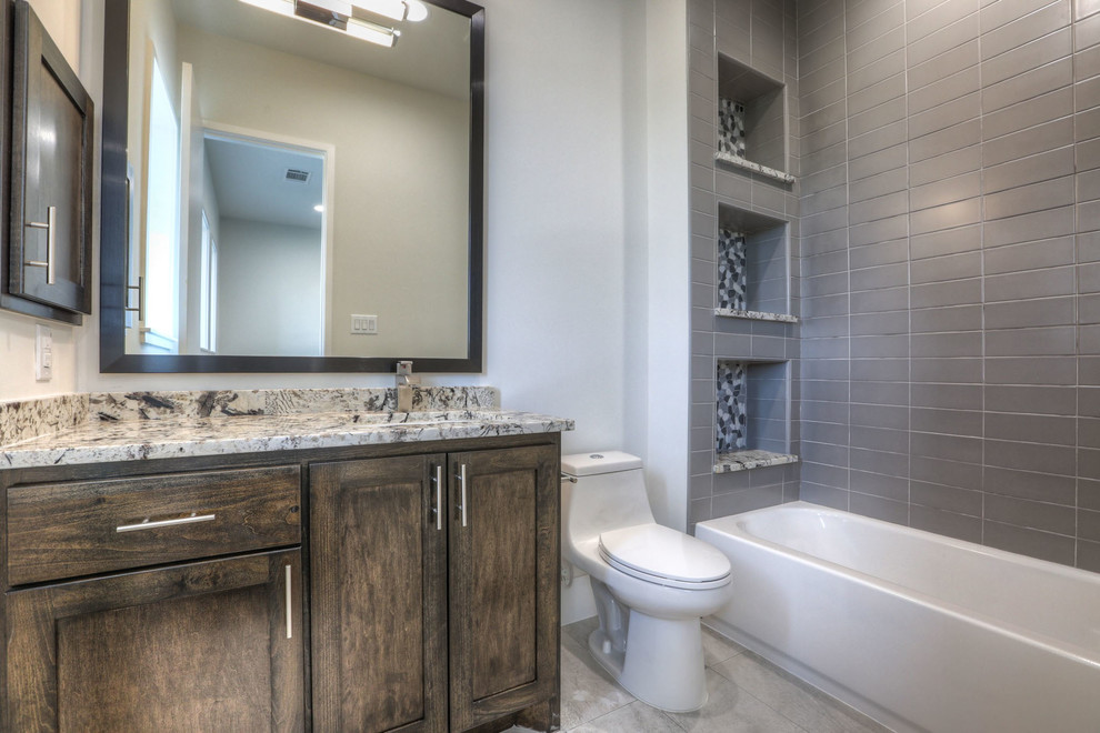 Bild på ett mellanstort funkis badrum, med luckor med infälld panel, skåp i mörkt trä, ett badkar i en alkov, en dusch/badkar-kombination, en toalettstol med hel cisternkåpa, grå kakel, keramikplattor, vita väggar, klinkergolv i keramik, ett undermonterad handfat, granitbänkskiva, grått golv och dusch med duschdraperi