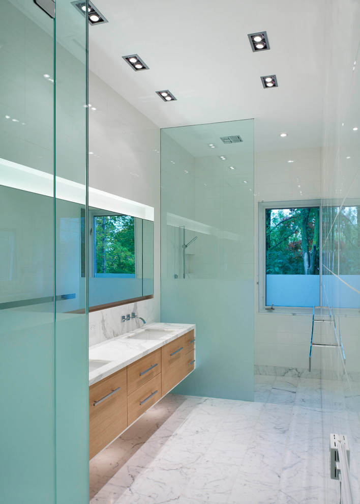 Inredning av ett modernt mellanstort badrum med dusch, med ett undermonterad handfat, släta luckor, skåp i ljust trä, en kantlös dusch, vit kakel, marmorbänkskiva, en toalettstol med hel cisternkåpa, keramikplattor, vita väggar, marmorgolv, vitt golv och med dusch som är öppen