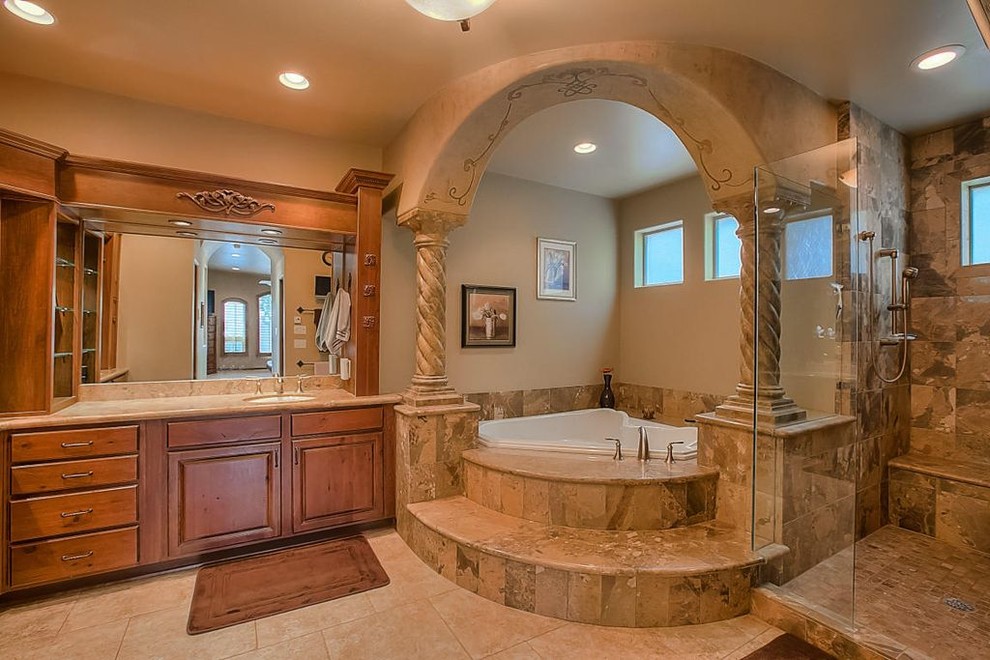 Cette image montre une douche en alcôve principale sud-ouest américain en bois brun de taille moyenne avec un placard avec porte à panneau surélevé, une baignoire posée, un carrelage beige, un carrelage de pierre, un mur beige, un sol en calcaire, un lavabo encastré et un plan de toilette en granite.