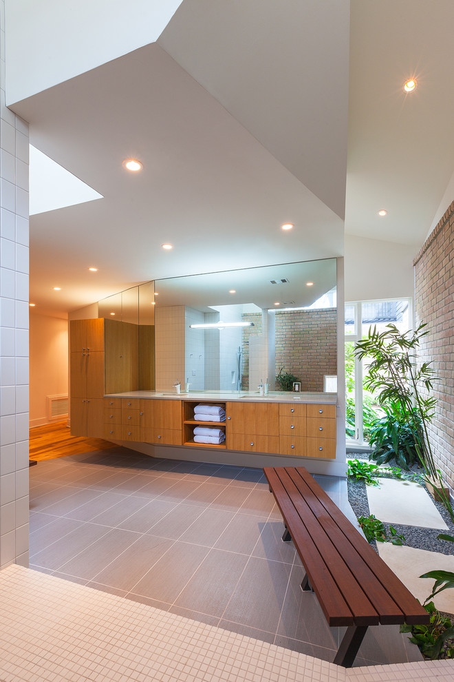 На фото: большая главная ванная комната в современном стиле с светлыми деревянными фасадами, плоскими фасадами, ванной в нише, белой плиткой, керамической плиткой, бежевыми стенами, полом из керамической плитки, врезной раковиной и столешницей из гранита