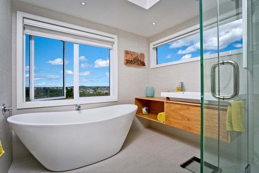 Photo of a contemporary bathroom in Auckland with medium wood cabinets, a freestanding bath, grey walls and a trough sink.