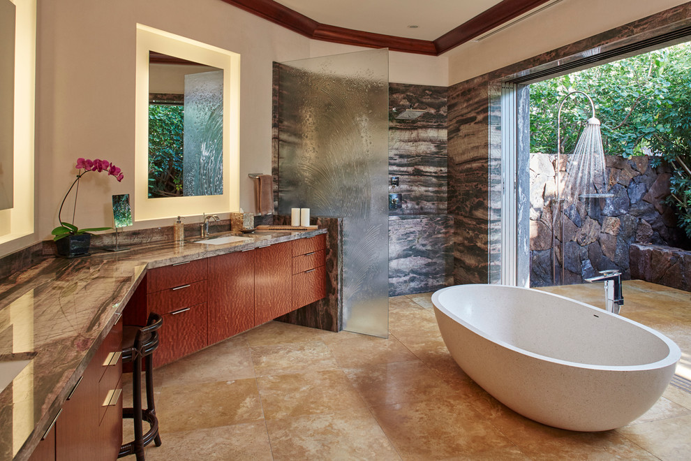 Inspiration for a large world-inspired ensuite bathroom in Hawaii with a submerged sink, freestanding cabinets, dark wood cabinets, granite worktops, a freestanding bath, a walk-in shower, a one-piece toilet, stone tiles, travertine flooring and brown walls.