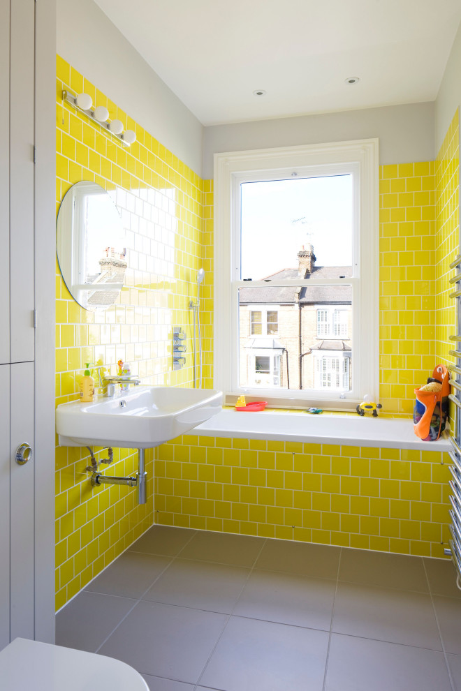 Idéer för ett litet badrum för barn, med ett badkar i en alkov, en dusch/badkar-kombination, en toalettstol med hel cisternkåpa, gul kakel, keramikplattor, grå väggar, klinkergolv i porslin, ett väggmonterat handfat och grått golv