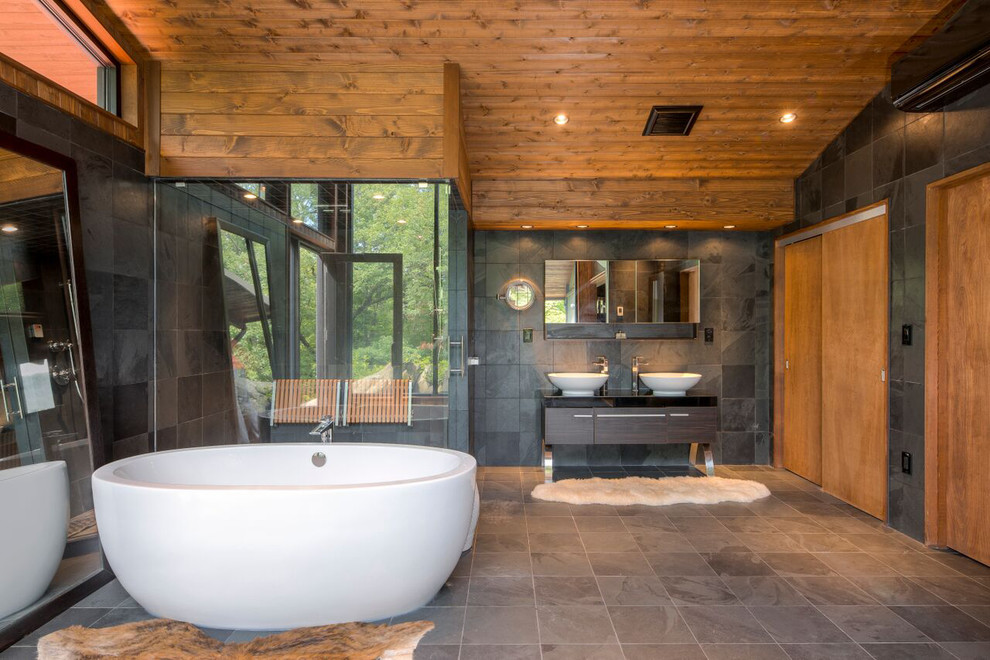 Inspiration pour une salle de bain principale design avec une baignoire indépendante, un carrelage gris, un carrelage de pierre, un mur gris, un sol en ardoise, une vasque, une douche d'angle, un sol marron et une cabine de douche à porte battante.