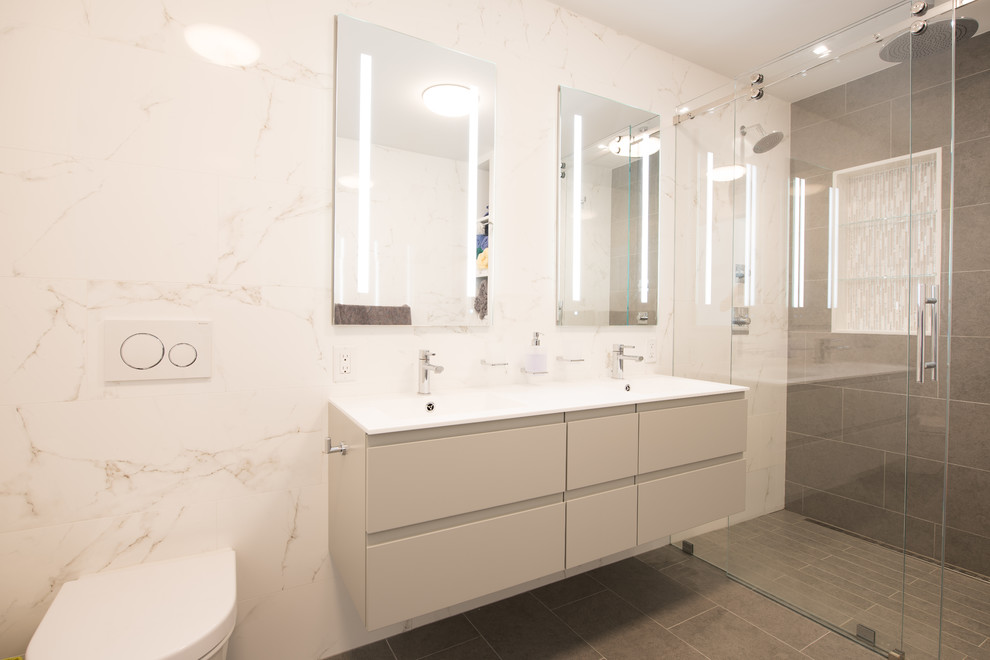 Photo of a large modern ensuite bathroom in New York with flat-panel cabinets, white cabinets, grey floors, a built-in shower, a wall mounted toilet, white tiles, cement tiles, white walls, an integrated sink, glass worktops, a sliding door, white worktops and ceramic flooring.