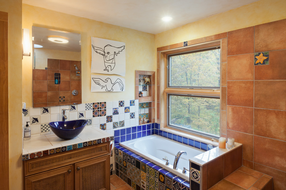 Cette image montre une salle de bain bohème en bois brun avec un placard avec porte à panneau encastré, une baignoire posée, un carrelage bleu, un carrelage multicolore, un carrelage orange, un mur jaune, une vasque et un plan de toilette en carrelage.