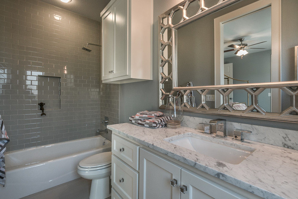 This is an example of a contemporary bathroom in Austin with shaker cabinets, white cabinets, an alcove bath, a shower/bath combination, a two-piece toilet, grey tiles, metro tiles, beige walls, a submerged sink, quartz worktops and a shower curtain.