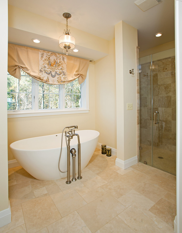 Klassisk inredning av ett en-suite badrum, med möbel-liknande, beige skåp, ett fristående badkar, en kantlös dusch, beige kakel, travertinkakel, gula väggar, klinkergolv i porslin, ett undermonterad handfat, granitbänkskiva, beiget golv och dusch med gångjärnsdörr