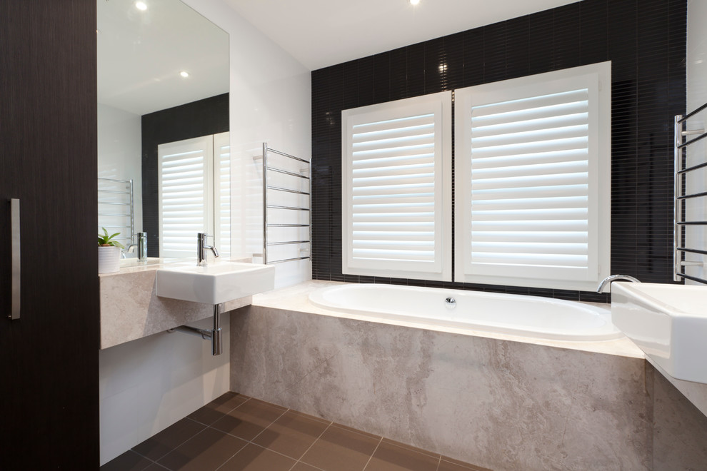 На фото: ванная комната в современном стиле с ванной в нише, черной плиткой, коричневой плиткой, белой плиткой, разноцветными стенами, подвесной раковиной и столешницей из известняка с