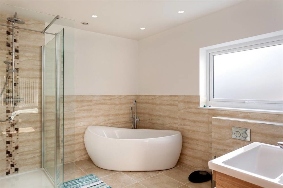Modernes Badezimmer En Suite mit flächenbündigen Schrankfronten, hellbraunen Holzschränken, offener Dusche, beigen Fliesen, beigem Boden, Falttür-Duschabtrennung, Eckbadewanne, Keramikboden und Einbauwaschbecken in Sussex