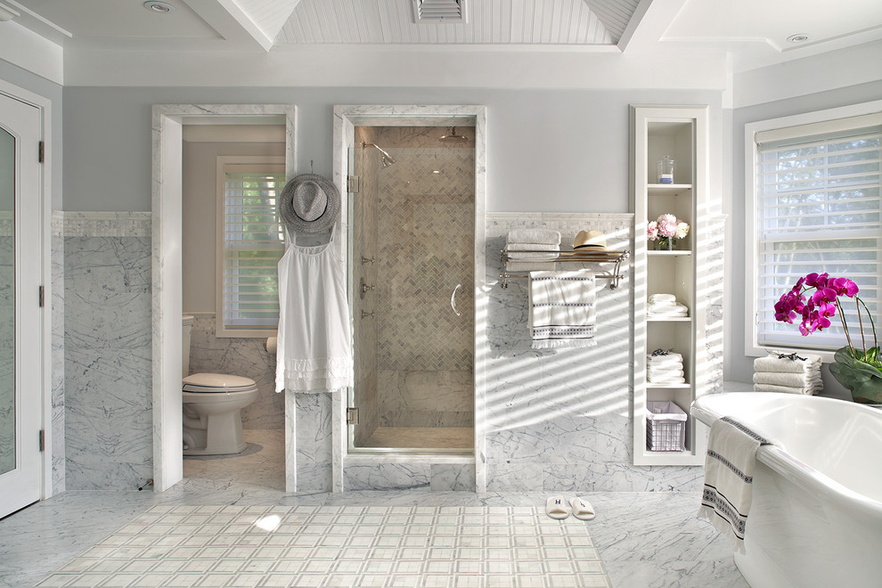 На фото: большая главная ванная комната в классическом стиле с открытыми фасадами, белыми фасадами, отдельно стоящей ванной, душем в нише, раздельным унитазом, серой плиткой, белой плиткой, каменной плиткой, серыми стенами и душем с распашными дверями