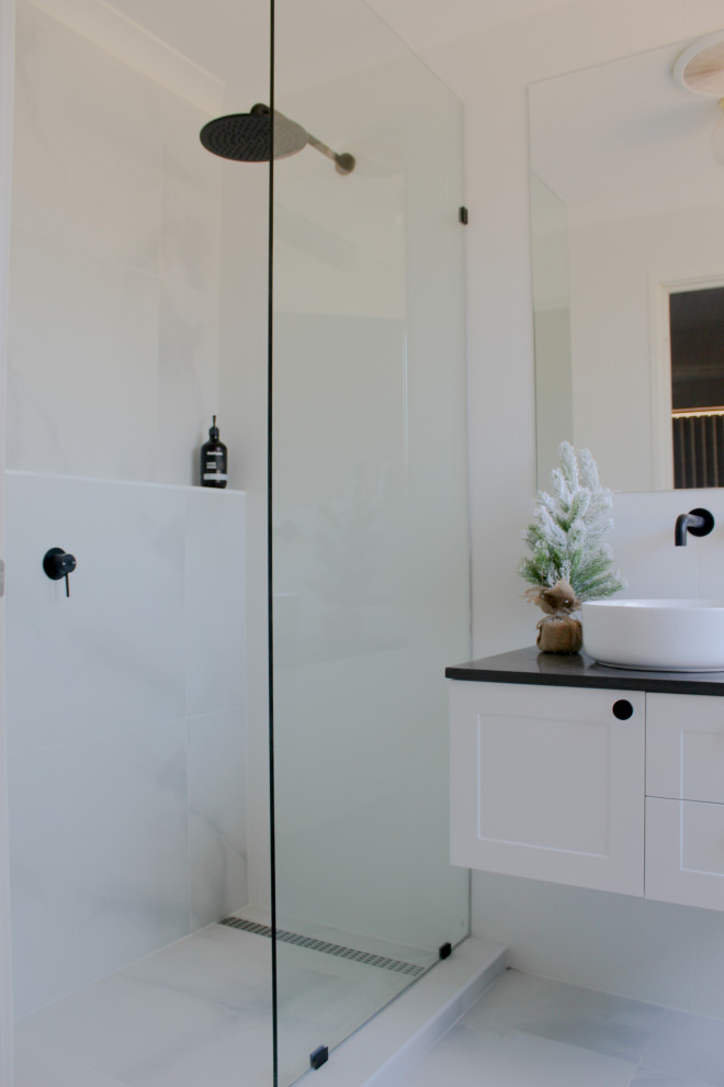 Photo of a small modern ensuite bathroom in Perth with shaker cabinets, white cabinets, a walk-in shower, a two-piece toilet, white tiles, porcelain tiles, white walls, porcelain flooring, a vessel sink, engineered stone worktops, white floors, an open shower and grey worktops.
