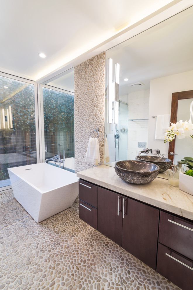 Inspiration for a small contemporary ensuite bathroom in Los Angeles with flat-panel cabinets, brown cabinets, a freestanding bath, a built-in shower, a wall mounted toilet, beige tiles, pebble tiles, beige walls, terrazzo flooring, a vessel sink, marble worktops, beige floors, a sliding door and beige worktops.