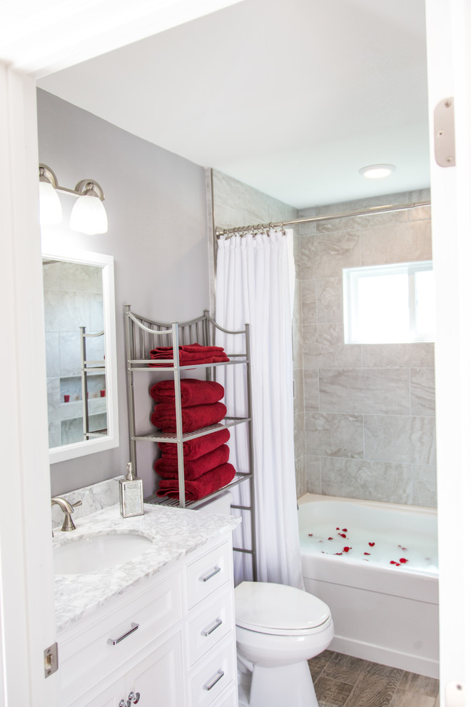 Cette image montre une petite salle de bain principale traditionnelle avec un placard à porte shaker, des portes de placard blanches, une baignoire en alcôve, un combiné douche/baignoire, WC séparés, un carrelage gris, des carreaux de porcelaine, un mur gris, un sol en vinyl, un lavabo encastré, un plan de toilette en quartz, un sol marron et une cabine de douche avec un rideau.