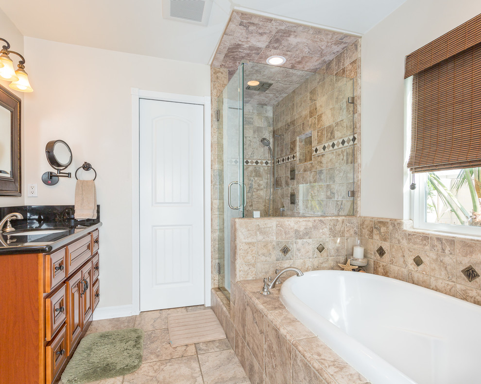 Medium sized beach style ensuite bathroom in Orange County with an alcove bath, a corner shower, ceramic tiles, shaker cabinets, brown cabinets, beige tiles, beige walls, ceramic flooring, a submerged sink, beige floors, a hinged door and black worktops.