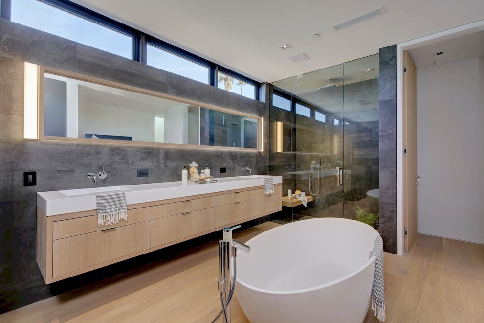 Foto på ett funkis vit en-suite badrum, med släta luckor, skåp i ljust trä, ett fristående badkar, en dusch i en alkov, grå kakel, grå väggar, mellanmörkt trägolv, ett integrerad handfat och brunt golv