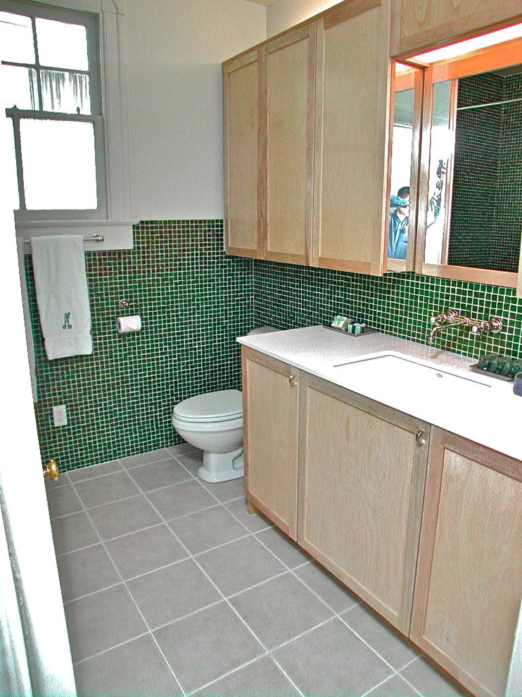 Réalisation d'une petite salle de bain bohème en bois clair avec un lavabo encastré, un placard avec porte à panneau encastré, un plan de toilette en surface solide, une baignoire en alcôve, un combiné douche/baignoire, WC séparés, un carrelage vert, un carrelage en pâte de verre, un mur blanc et un sol en carrelage de porcelaine.