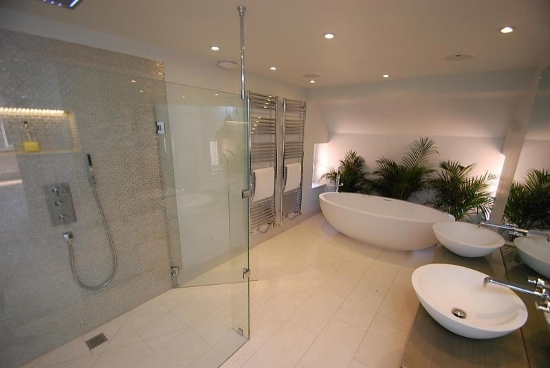 Large contemporary ensuite bathroom in Surrey with a vessel sink, freestanding cabinets, light wood cabinets, glass worktops, a freestanding bath, a built-in shower, beige tiles, mosaic tiles, white walls and travertine flooring.
