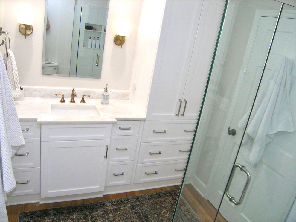 Photo of a medium sized contemporary family bathroom in Tampa with shaker cabinets, white cabinets, a corner shower, a two-piece toilet, white tiles, ceramic tiles, grey walls, light hardwood flooring, a submerged sink, engineered stone worktops, brown floors, a hinged door, grey worktops, a single sink and a built in vanity unit.