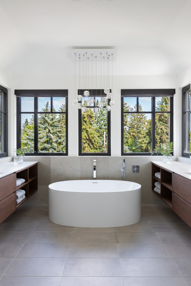 Идея дизайна: главная ванная комната в современном стиле с темными деревянными фасадами, отдельно стоящей ванной, белыми стенами, серым полом, белой столешницей, тумбой под две раковины и подвесной тумбой