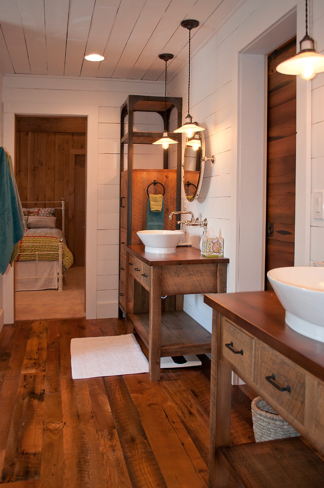 Modelo de cuarto de baño principal rústico de tamaño medio con armarios tipo mueble, puertas de armario de madera oscura, ducha esquinera, paredes blancas, lavabo sobreencimera y encimera de madera