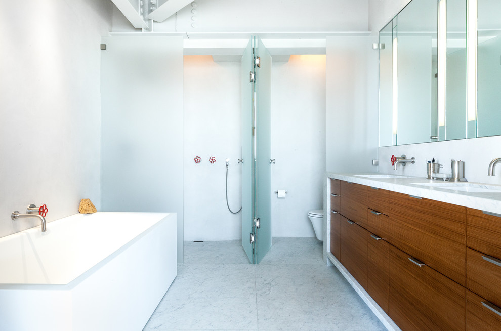 На фото: главная ванная комната в стиле лофт с врезной раковиной, плоскими фасадами, фасадами цвета дерева среднего тона, отдельно стоящей ванной, душем без бортиков и белыми стенами с
