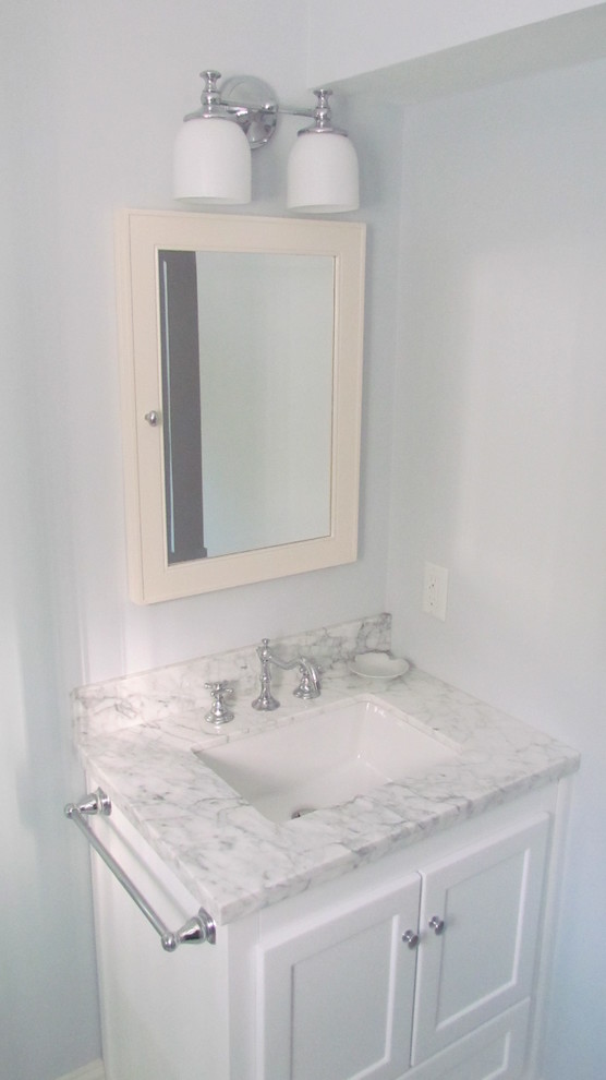 Пример оригинального дизайна: ванная комната в классическом стиле с подвесной раковиной, фасадами с утопленной филенкой, белыми фасадами, мраморной столешницей, угловым душем, унитазом-моноблоком, белой плиткой, керамогранитной плиткой, серыми стенами, полом из керамогранита и душевой кабиной