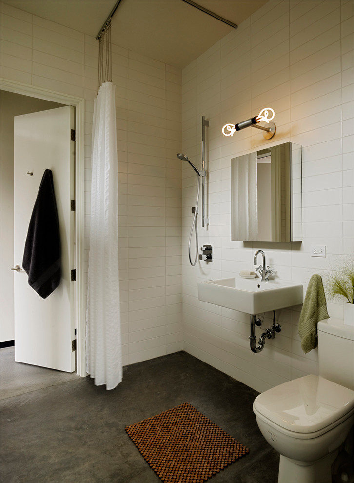На фото: большая ванная комната в стиле модернизм с угловым душем, унитазом-моноблоком, белой плиткой, керамогранитной плиткой, белыми стенами, бетонным полом, душевой кабиной, подвесной раковиной и шторкой для ванной с