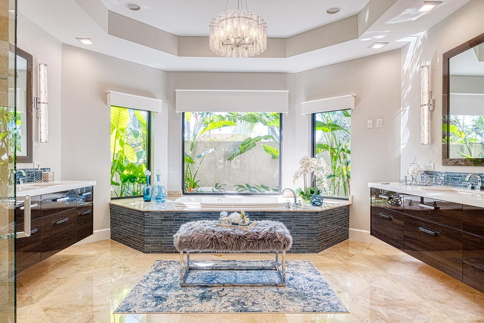 マイアミにある地中海スタイルのおしゃれなマスターバスルーム (フラットパネル扉のキャビネット、濃色木目調キャビネット、ドロップイン型浴槽、青いタイル、ベージュの壁、アンダーカウンター洗面器、ベージュの床、白い洗面カウンター) の写真