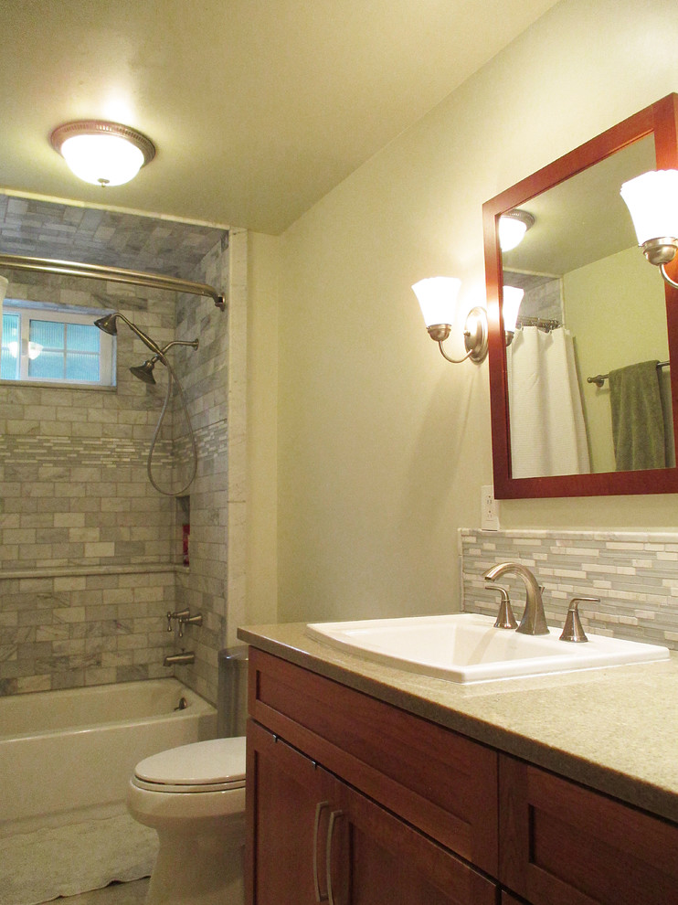 Photo of a medium sized classic shower room bathroom in Seattle with a built-in sink, shaker cabinets, medium wood cabinets, solid surface worktops, an alcove bath, a two-piece toilet, white tiles, stone tiles, green walls, porcelain flooring and a shower/bath combination.