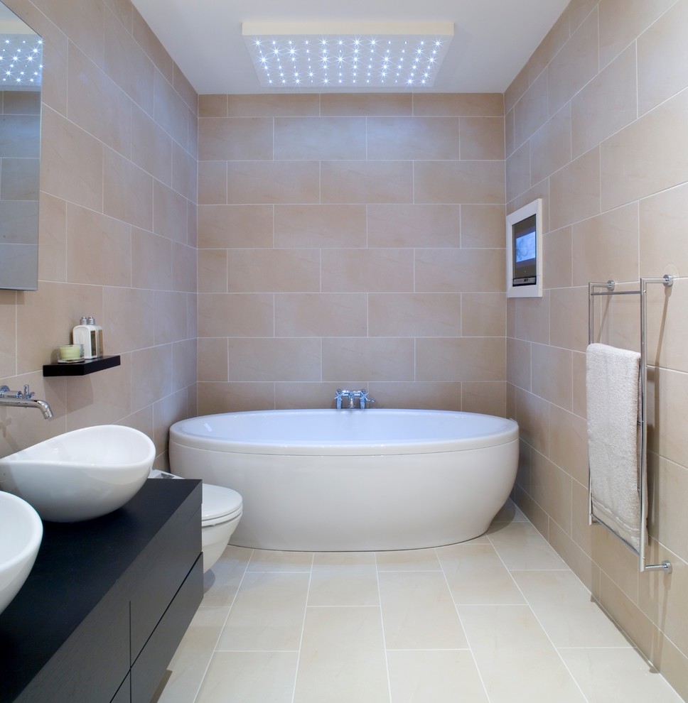 На фото: ванная комната: освещение в современном стиле с плоскими фасадами, черными фасадами, отдельно стоящей ванной, бежевыми стенами, бежевым полом и черной столешницей с