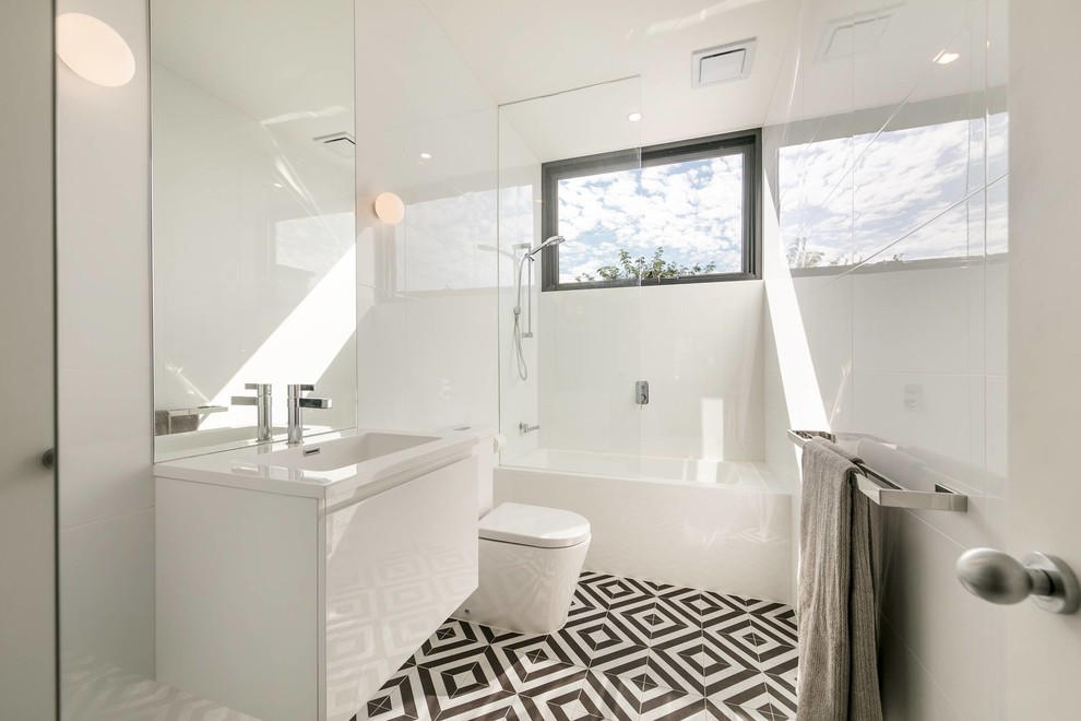 Réalisation d'une salle d'eau design avec un placard à porte plane, des portes de placard blanches, une baignoire en alcôve, un combiné douche/baignoire, un lavabo suspendu, un sol noir, un plan de toilette blanc et du carrelage bicolore.