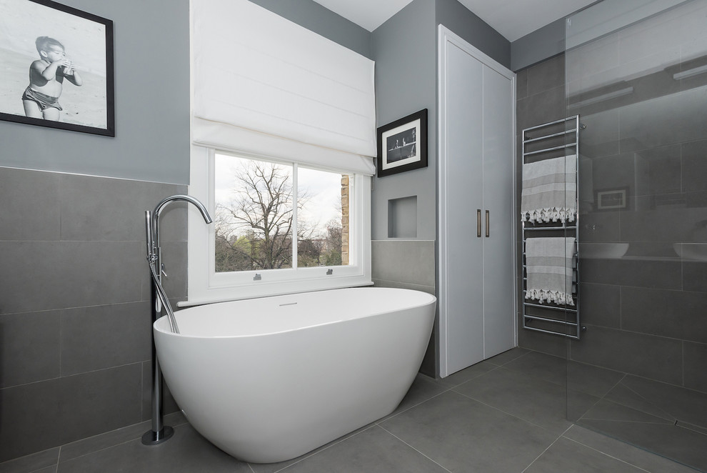 This is an example of a large modern family bathroom in London with blue cabinets, a freestanding bath, a shower/bath combination, a wall mounted toilet, grey tiles, ceramic tiles, green walls and ceramic flooring.